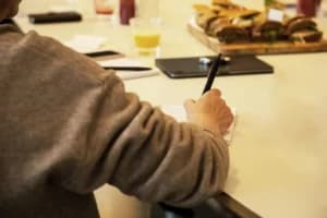 Close up van een hand die iets aan het noteren is tijdens een infosessie