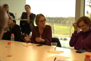 Een vrouw is iets aan het bespreken met de persoon die langs haar aan tafel zit