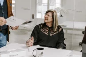 Liesbeth zit glimlachend aan een tafel tijdens een meeting