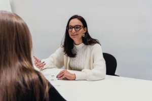 Iemand zit met een klant aan de tafel en geeft uitleg aan de persoon tegenover haar