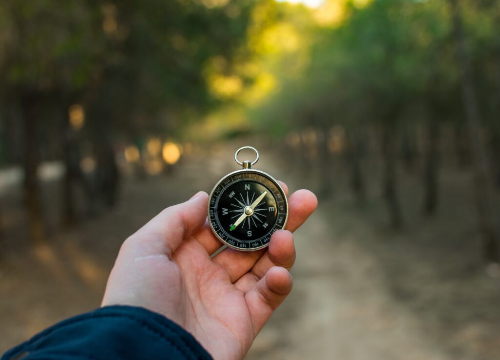 Han die een kompas vasthoud op een weg in het bos