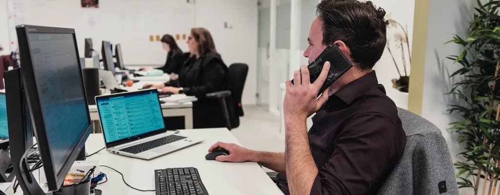 Iemand is druk aan het bellen met een gsm achter zijn bureau