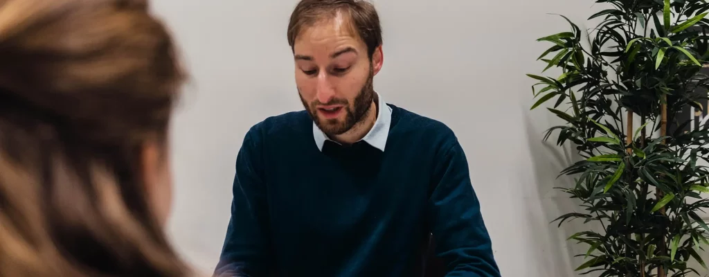 Medewerker van Motmans zit glimlachend aan tafel iets uit te leggen